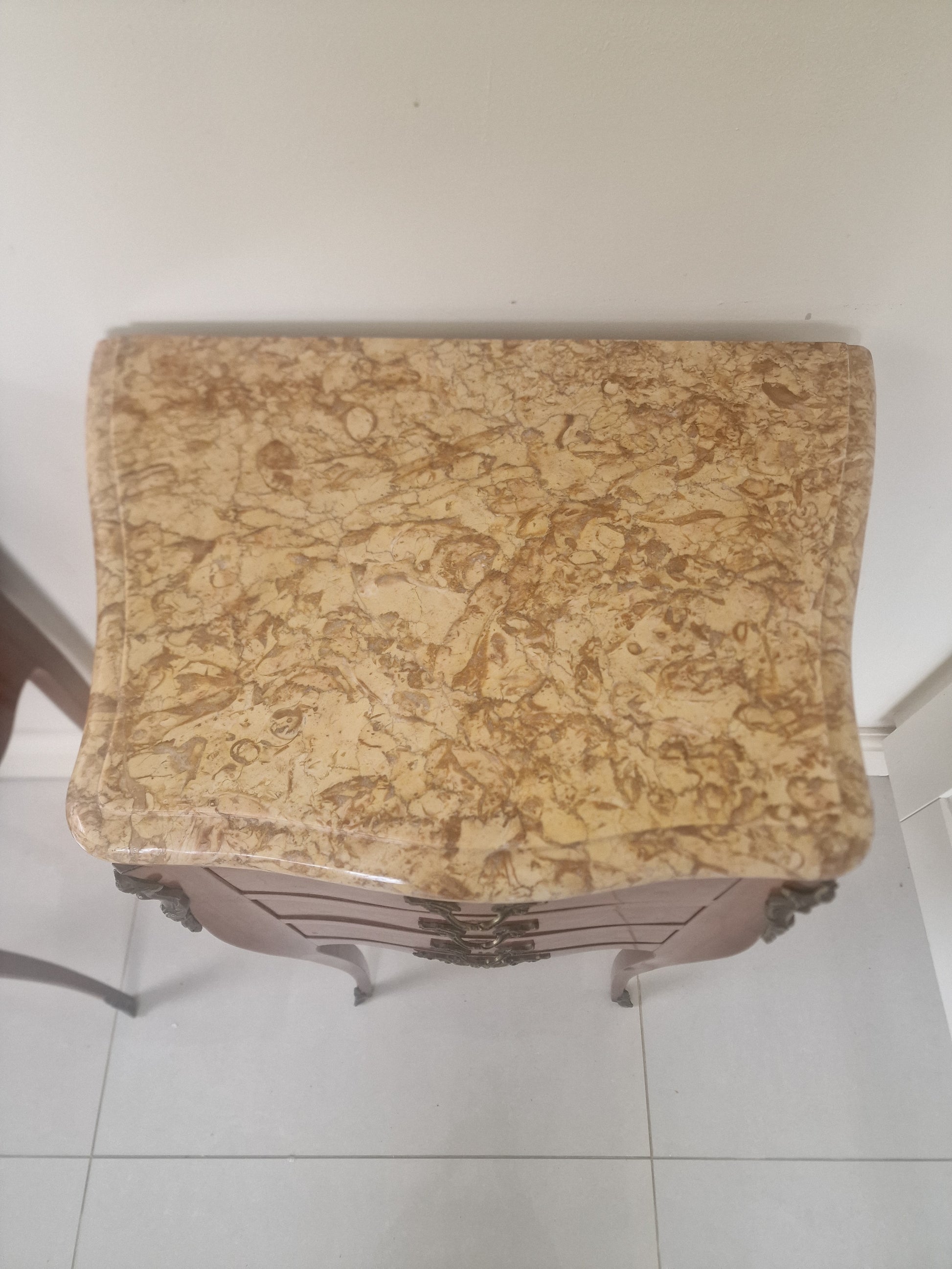 Marble top of Louis XV style wooden nightstand on a plain background