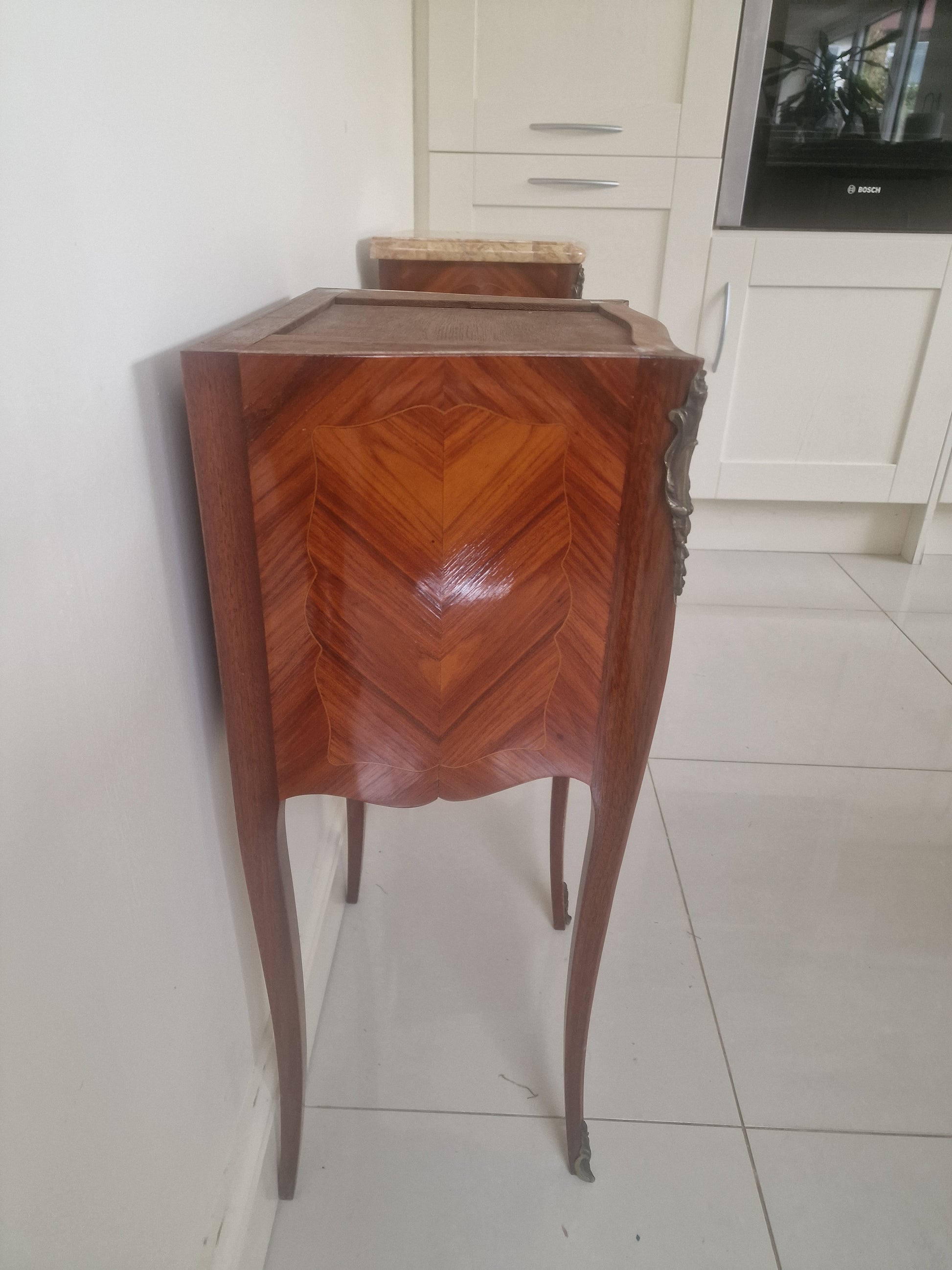 Side of Louis XV style wooden nightstands with marble tops on a plain background