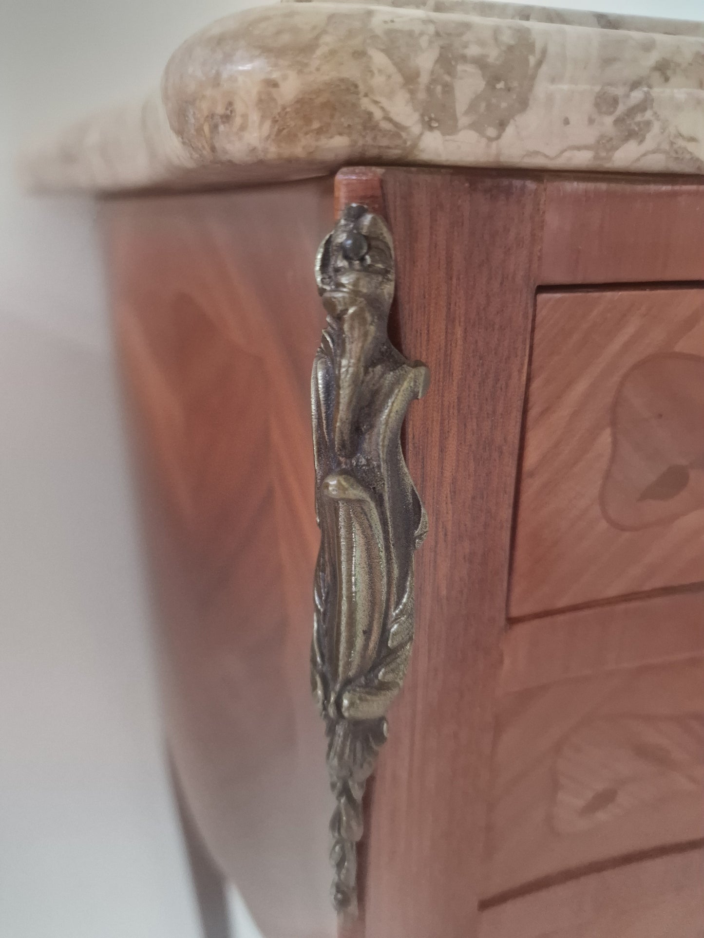 Close up of corner of French Louis XV style wooden nightstand with marble top on a plain background